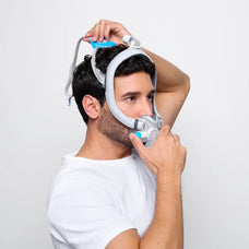 Man putting on the F30i CPAP mask, front first and attaching the back.
